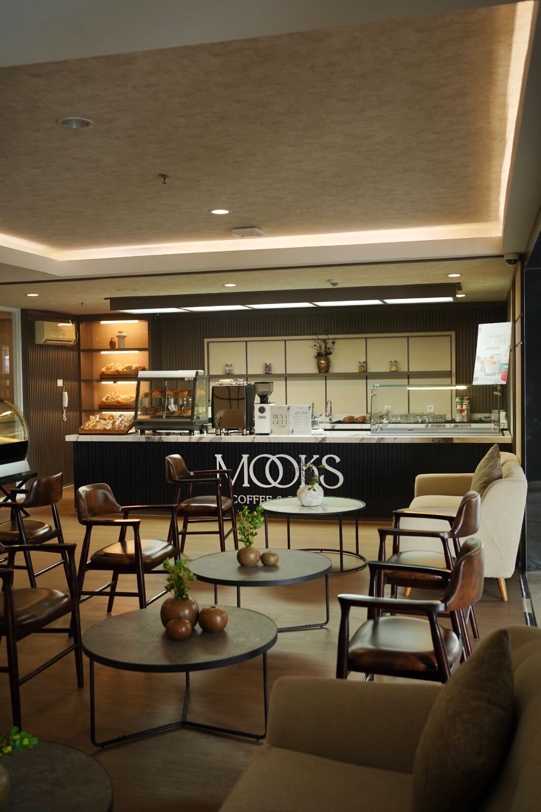 A modern coffee shop interior with seating, a counter displaying pastries, and a sign reading 'MOOKS COFFEE'.