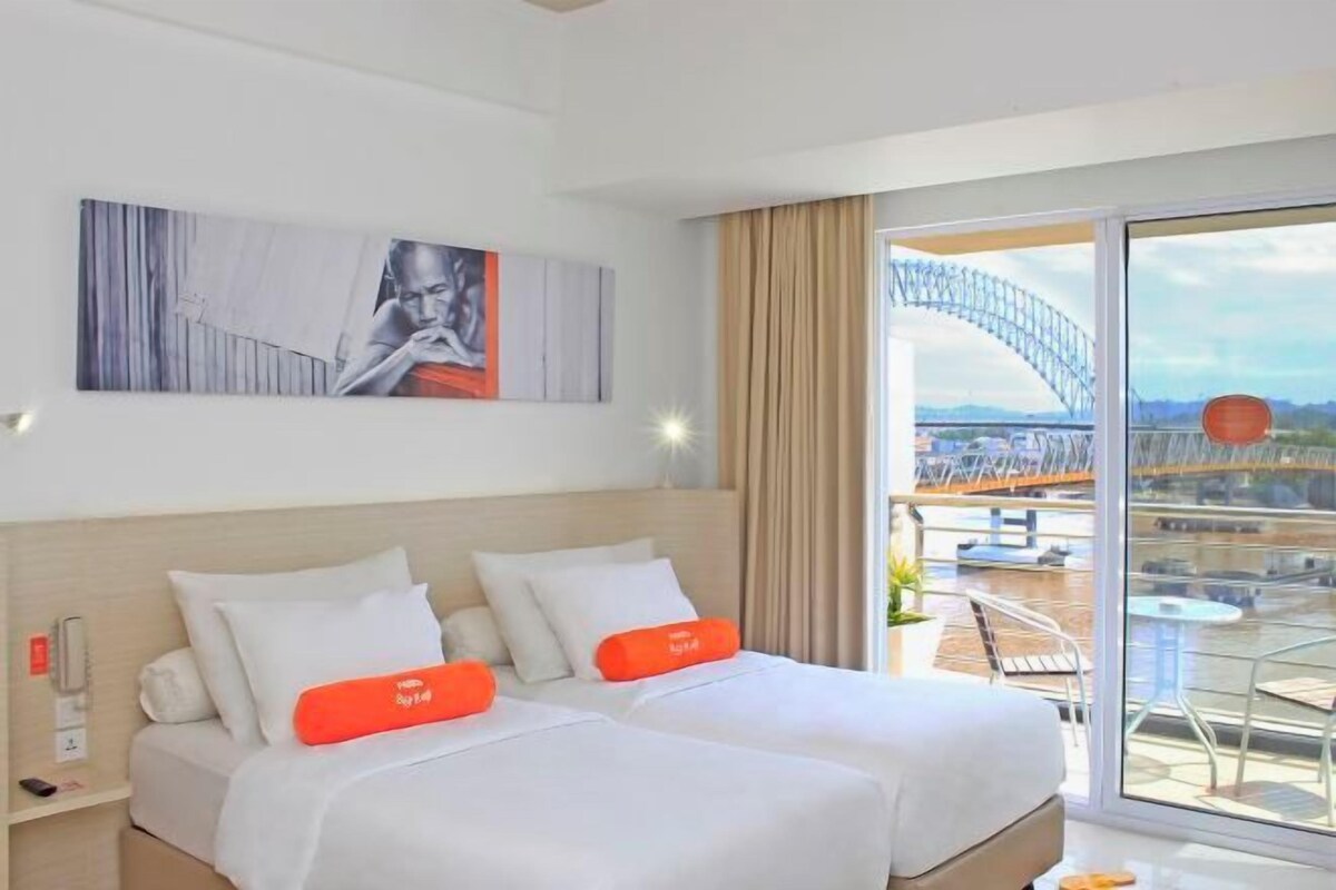 A hotel room with a bed, a painting on the wall, and a view of a bridge.