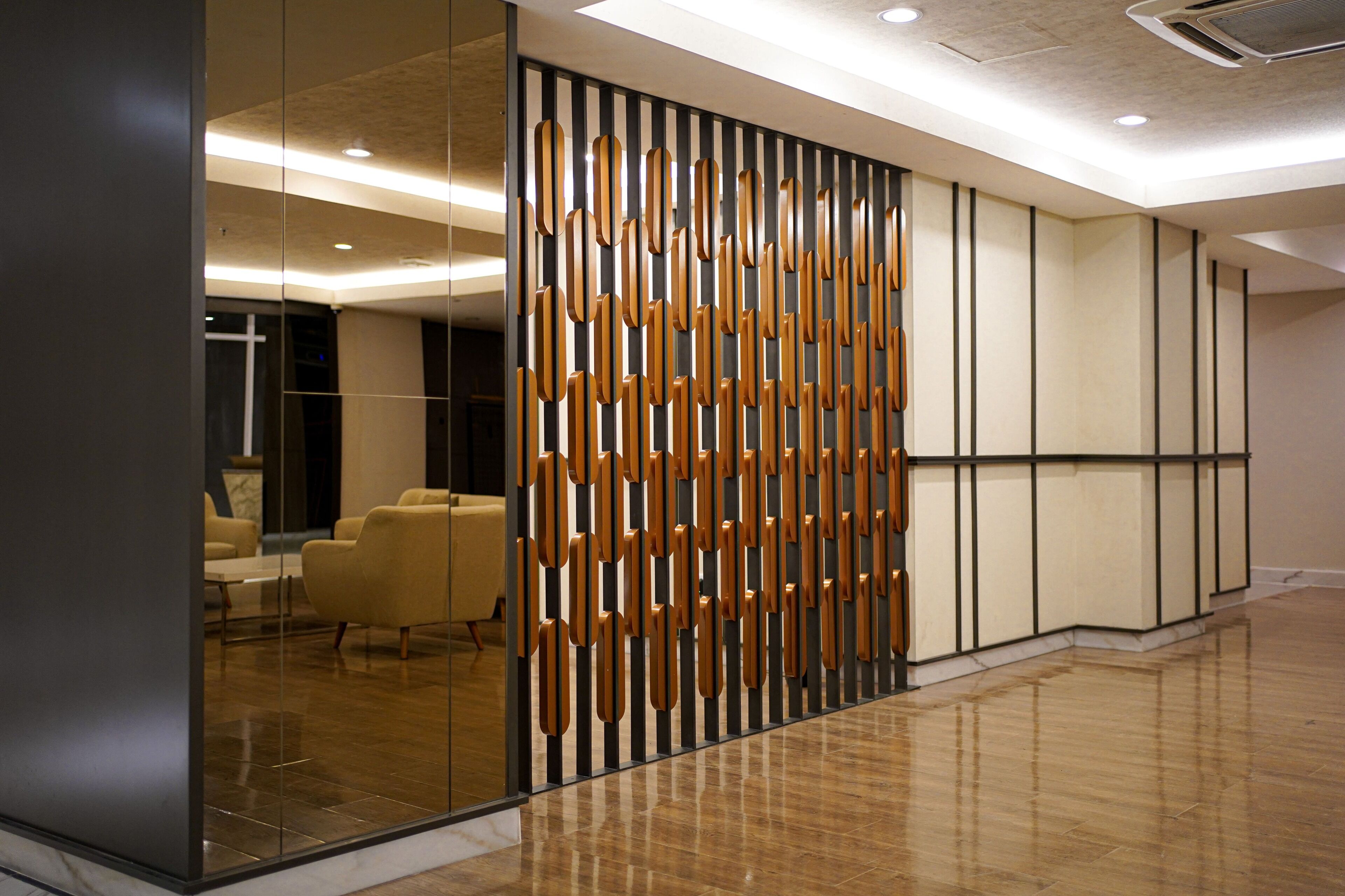 Een moderne hotel lobby met een decoratief houten paneel, een zithoek met stoelen, en een gepolijste houten vloer.