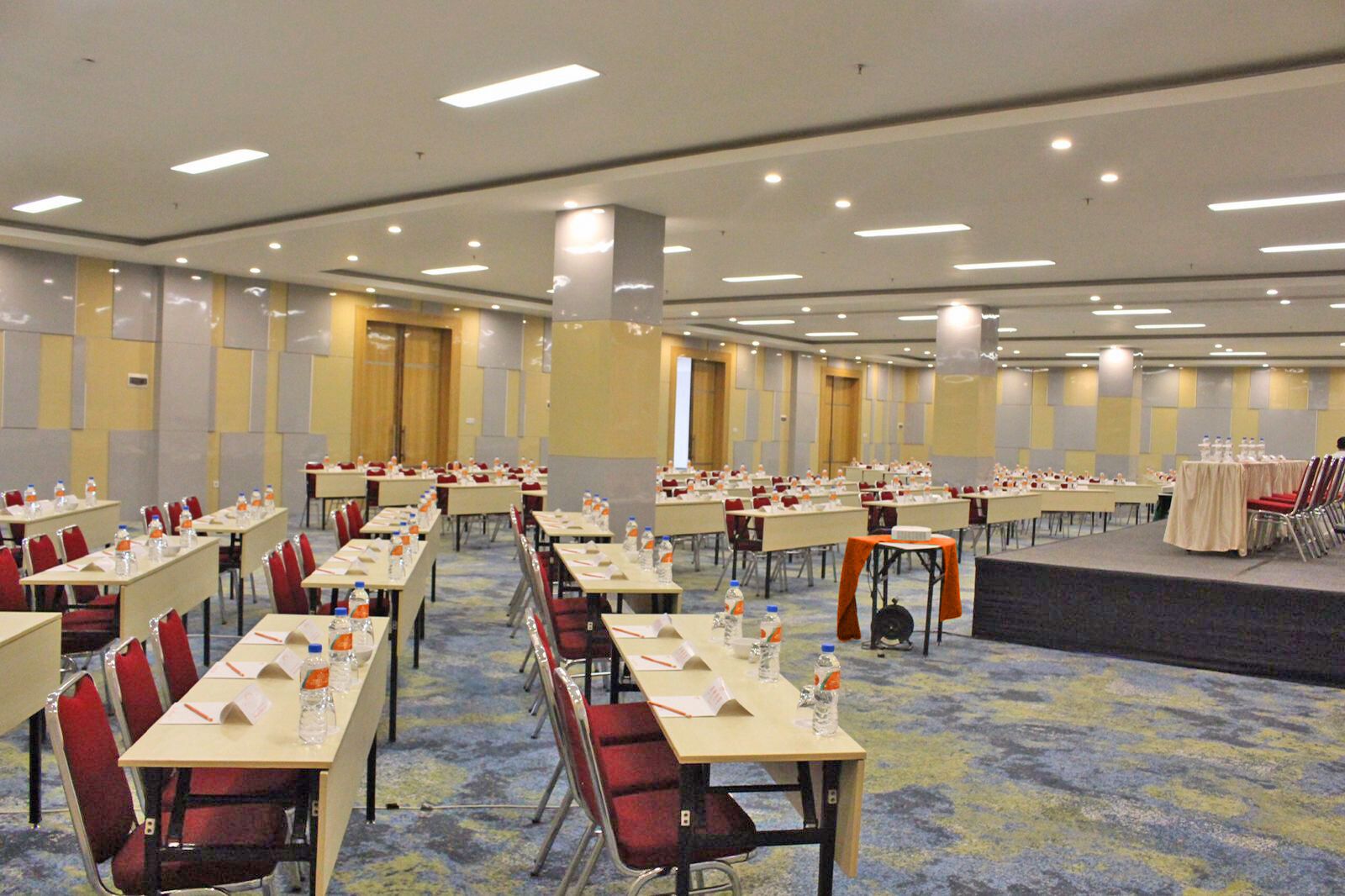 Un amplio salón de conferencias con filas de mesas y sillas, equipado con botellas de agua y tarjetas de identificación.