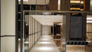 Un pasillo moderno de hotel con un separador de vidrio, suelo de mármol y un área de descanso con un sofá.