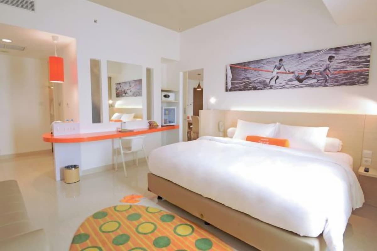 Habitación de hotel con una cama grande, un escritorio con silla, un cesto de basura pequeño y un cuadro en la pared.