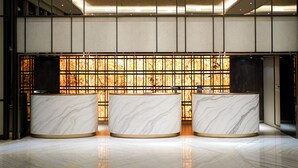 Un área de recepción con tres mostradores de mármol y una pared decorativa con diseño de cuadrícula.