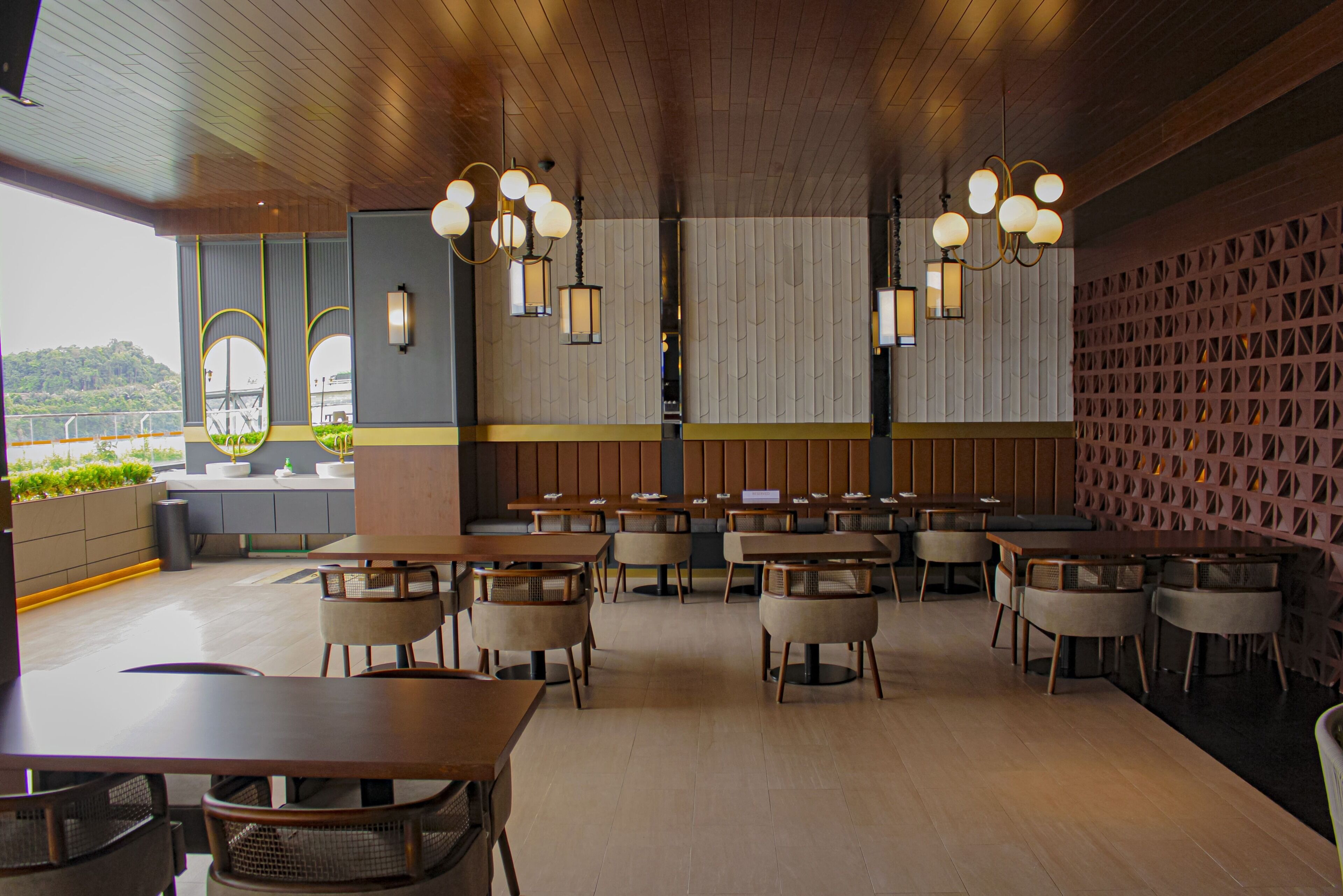 A restaurant with wooden tables and chairs, a high ceiling, and pendant lighting.