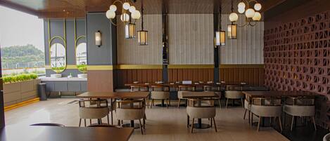A restaurant with wooden tables and chairs, a high ceiling, and pendant lighting.