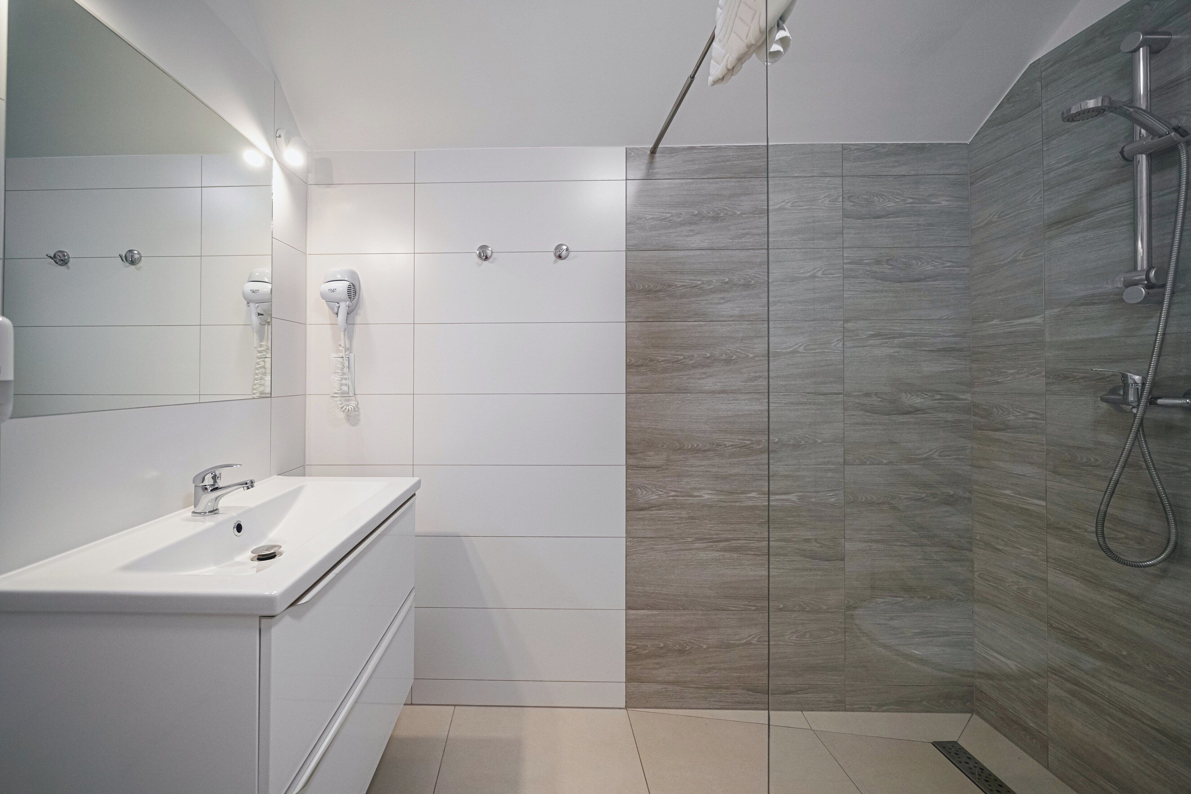 A modern bathroom with a white vanity, a large mirror, and a shower area with a wooden wall.