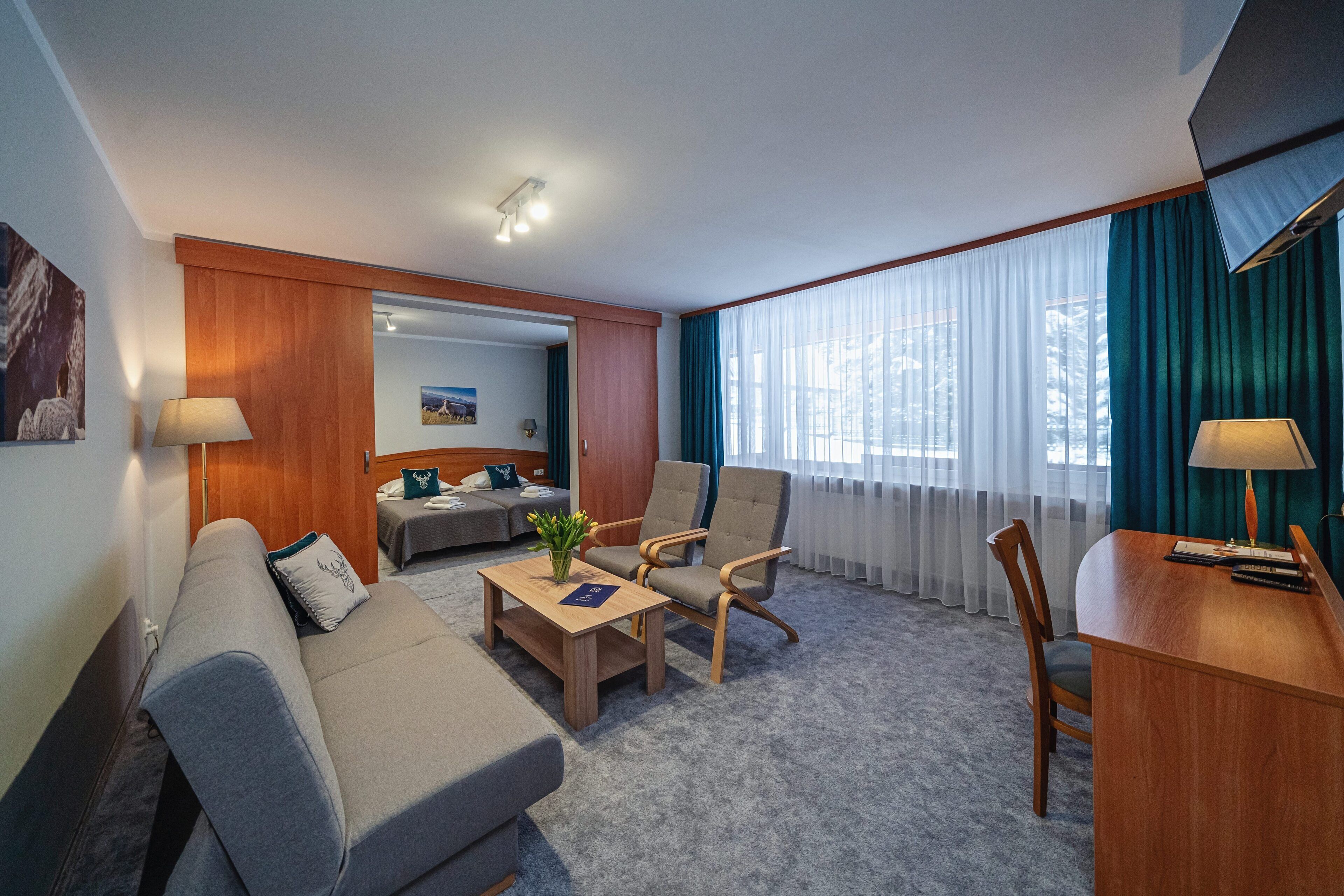 Een hotelkamer met een sofa, fauteuil, bureau en een bed met uitzicht op de stad.