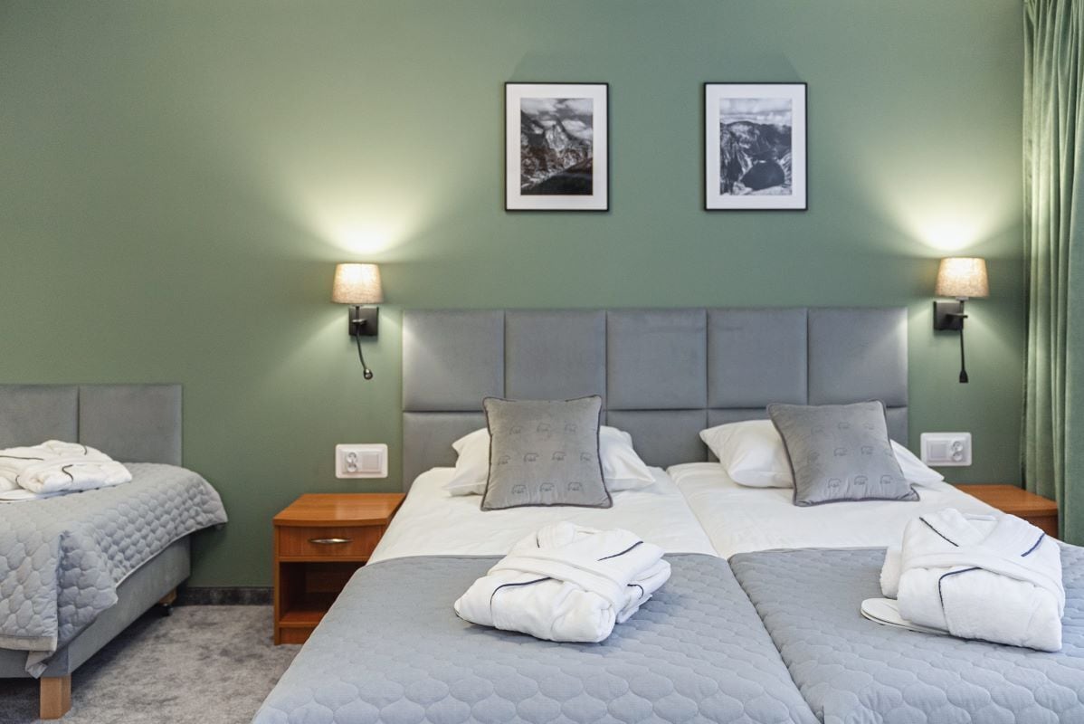 Habitación de hotel con dos camas, ropa de cama gris y dos lámparas de noche.