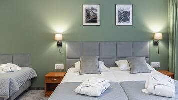 Habitación de hotel con dos camas, ropa de cama gris y dos lámparas de noche.