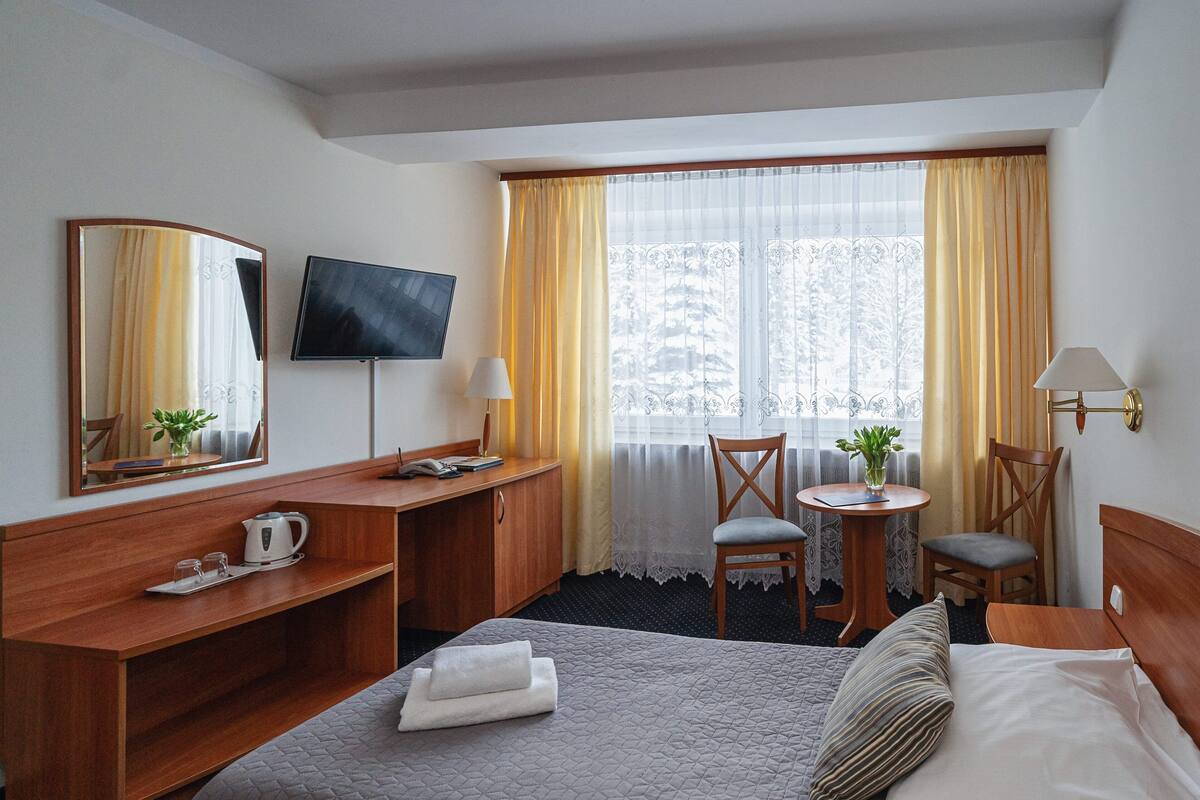 Een hotelkamer met een bed, een bureau, een stoel, een televisie en een raam met gordijnen.