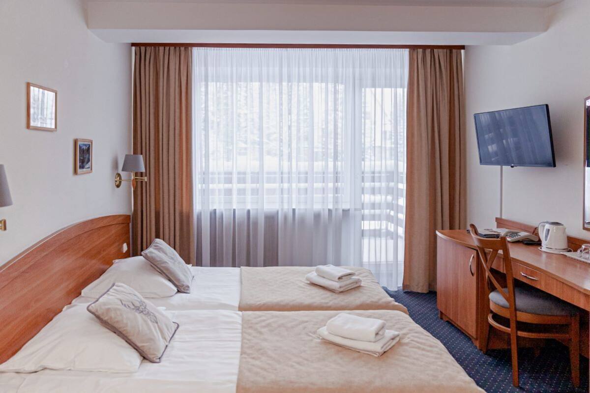 Een hotelkamer met twee bedden, een bureau, een stoel, een televisie en een raam met gordijnen.