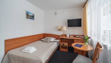 Ein Hotelzimmer mit Bett, Schreibtisch, Stuhl, Fernseher und einem kleinen Tisch mit Blumenvase.