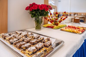 A buffet table with desserts and a vase of red roses.