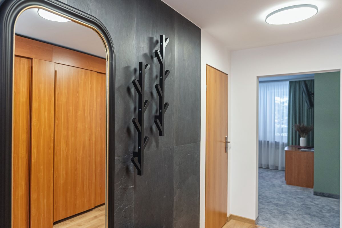 Un pasillo con un espejo que refleja un armario, una obra de arte abstracta colgada en la pared y una puerta que da a otra habitación.