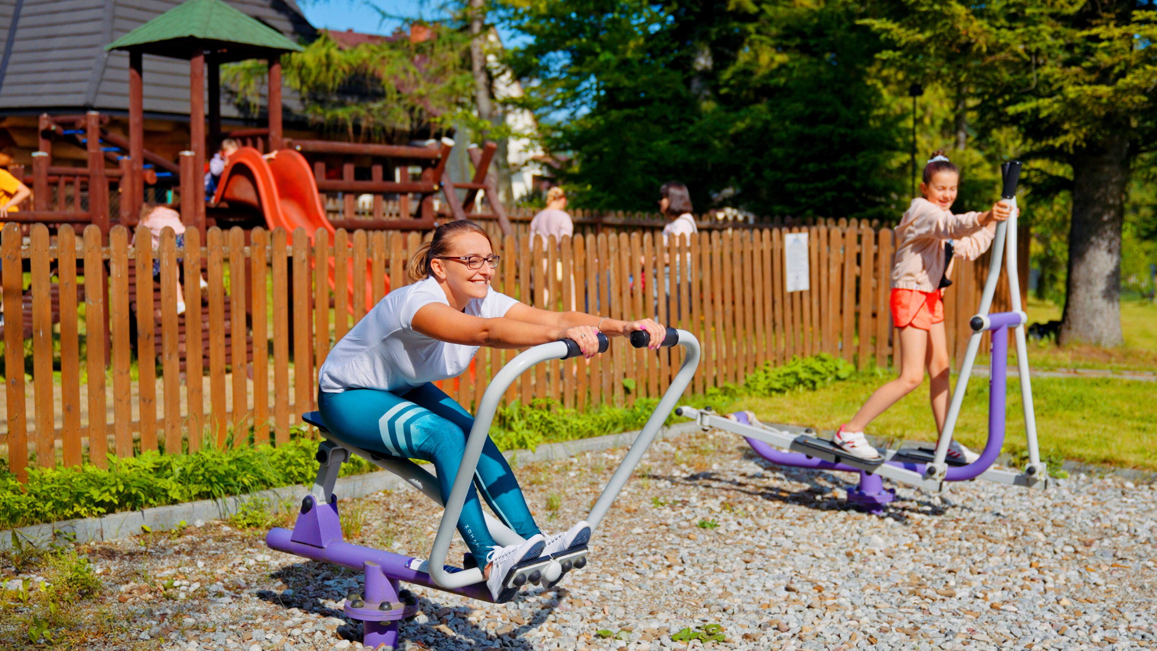 Two people exercising on outdoor fitness equipment in a park.