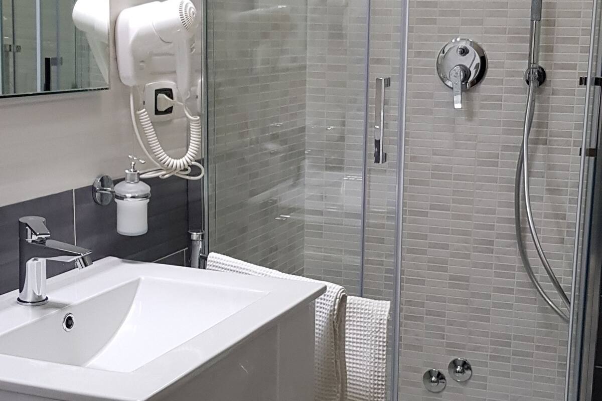 A modern bathroom with a glass-enclosed shower, a white sink, and a hairdryer mounted on the wall.