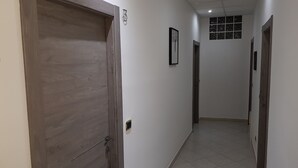 Un pasillo con una puerta de madera a la izquierda, piso de baldosas y una ventana con diseño de cuadrícula en la pared.