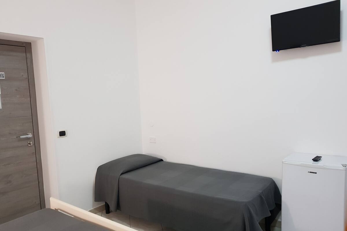 A small room with a bed, a desk, and a television on the wall.