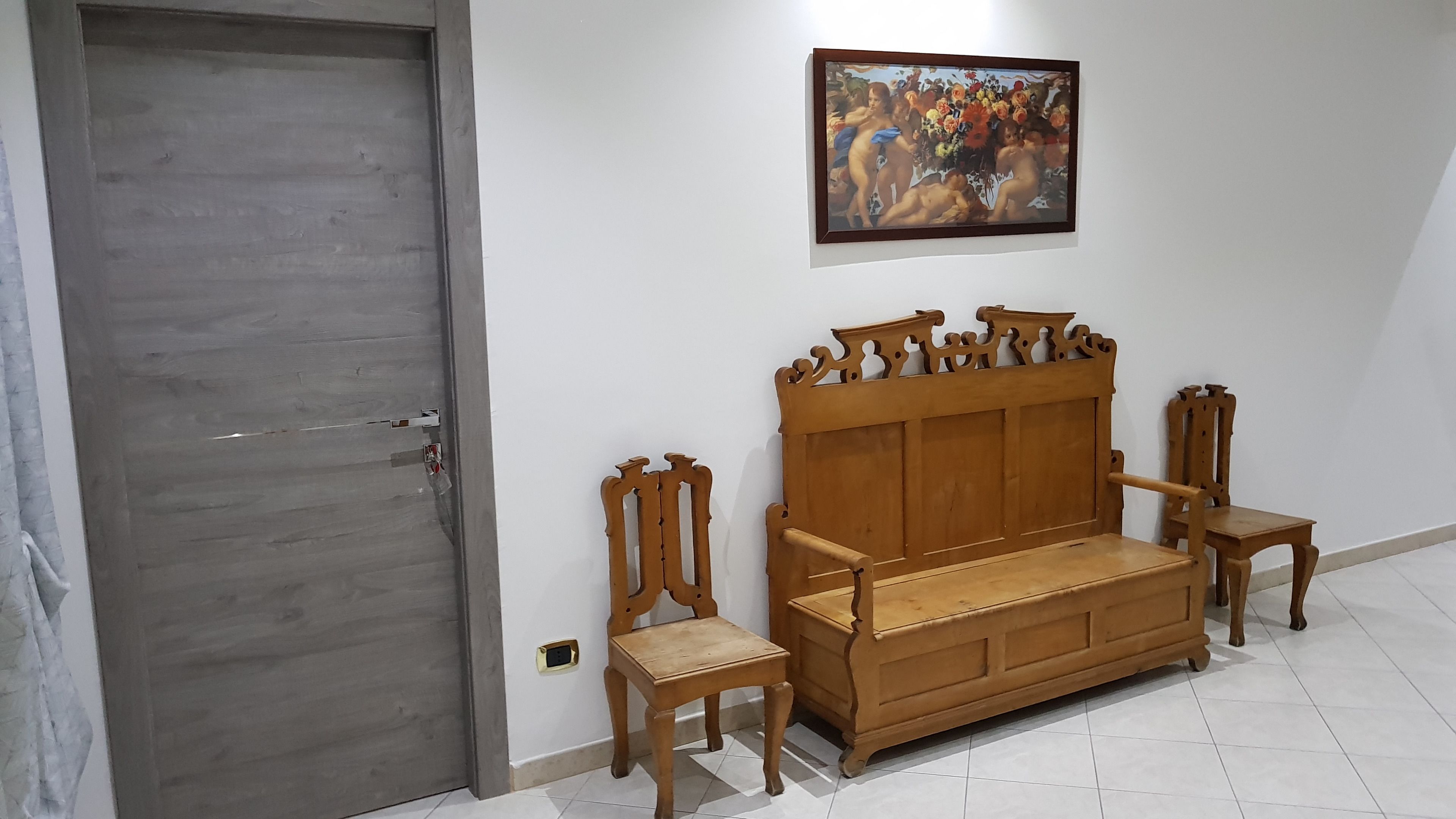 A room with a wooden door, a sofa, two chairs, and a painting on the wall.