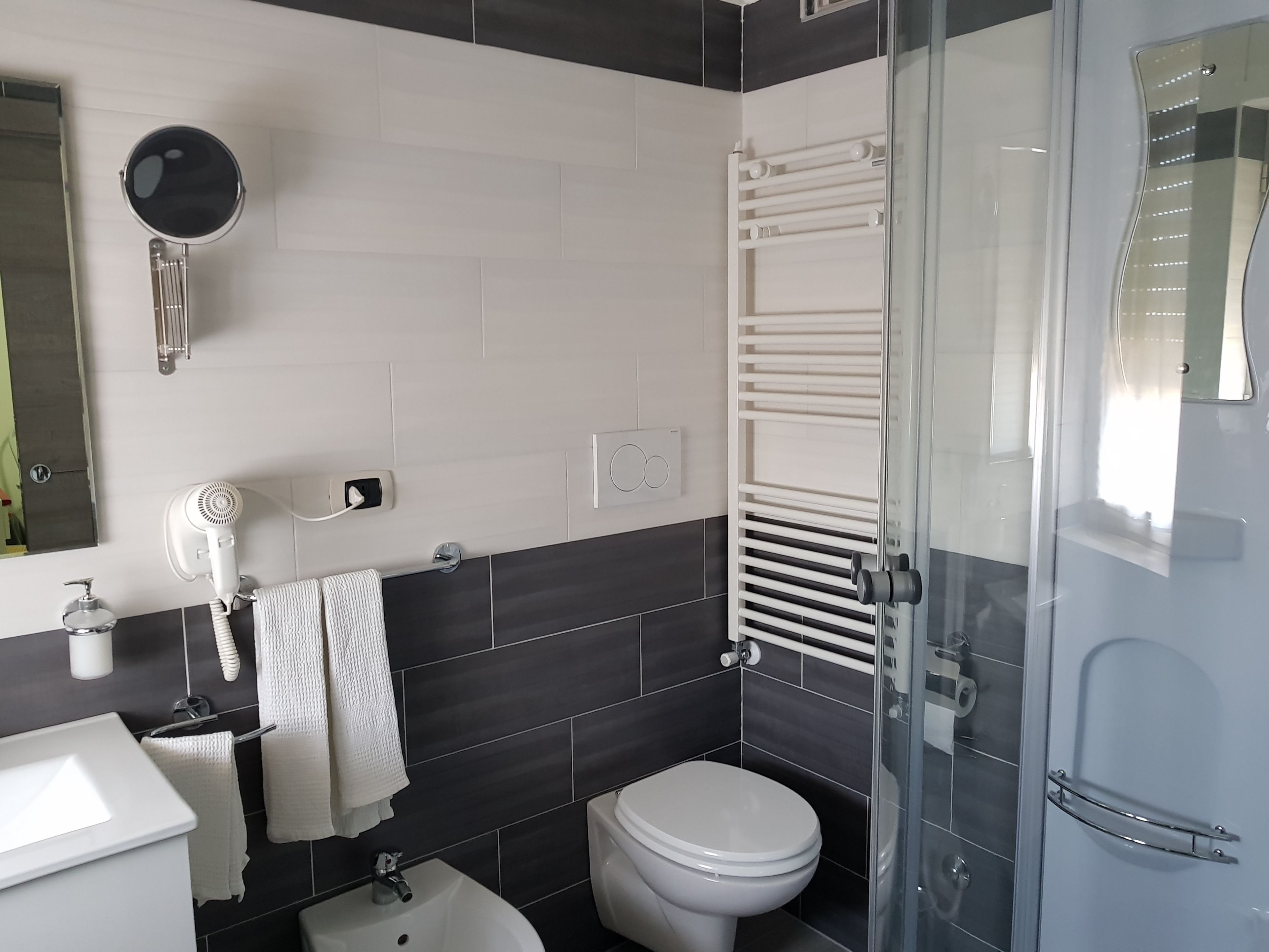 Un baño moderno con un lavabo blanco, un inodoro, un secador de pelo y una cabina de ducha de vidrio.