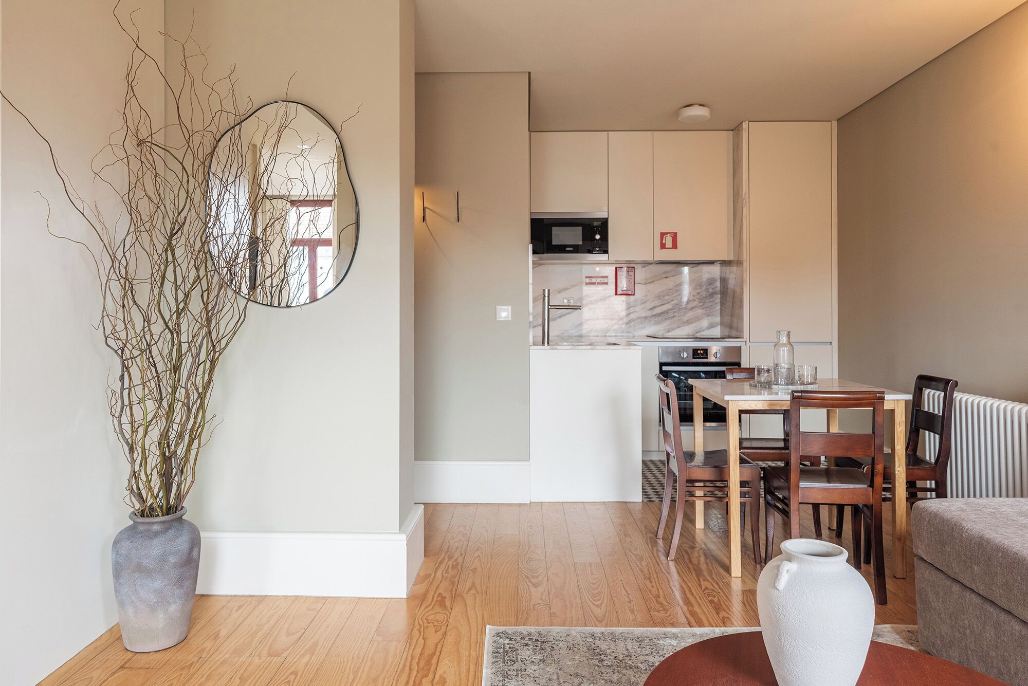 Une cuisine moderne avec des meubles blancs, un four à micro-ondes et un four en acier inoxydable. On y trouve une table à manger avec des chaises et un vase.