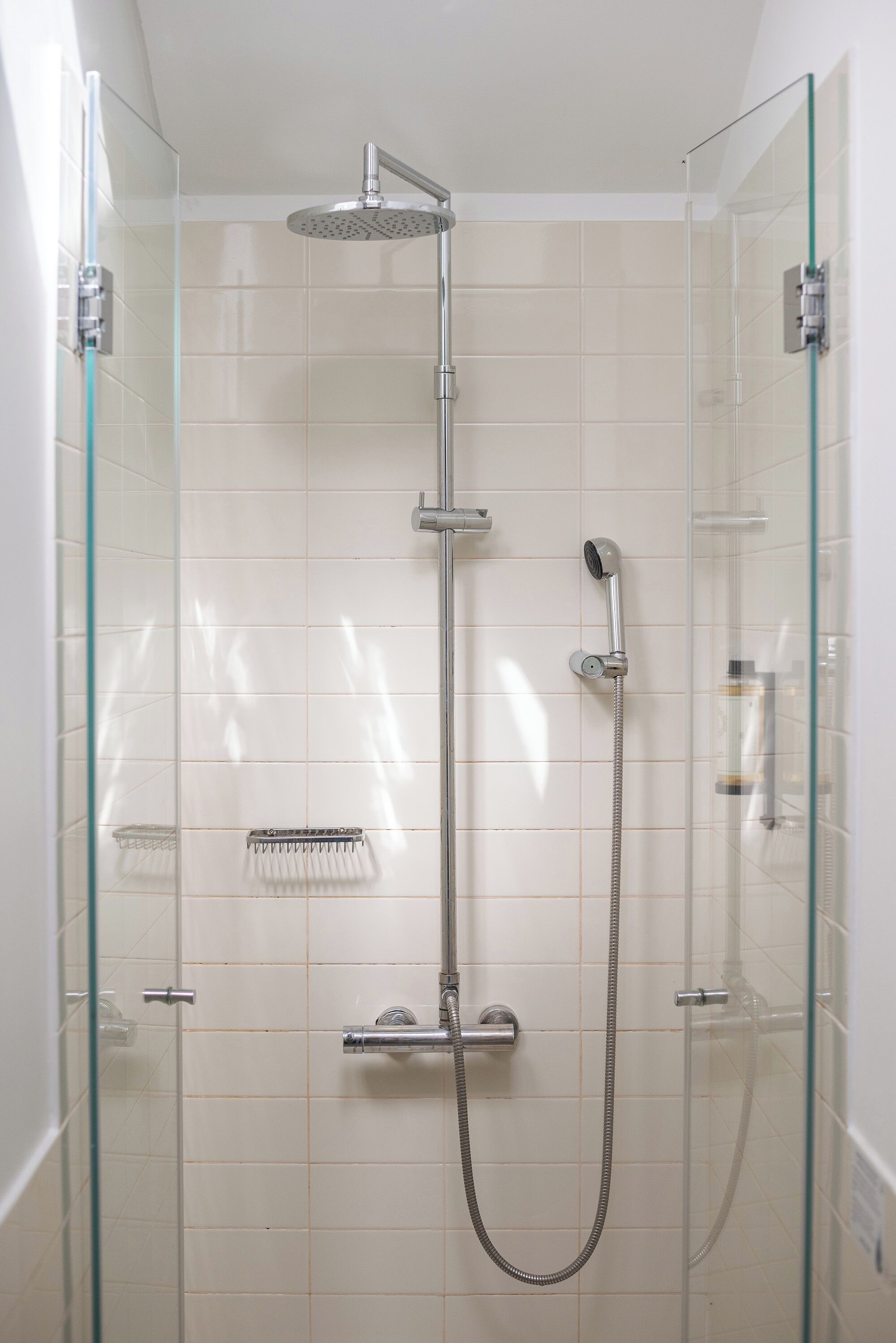 A glass-enclosed shower stall with a handheld showerhead, a wall-mounted faucet, and a handheld showerhead.