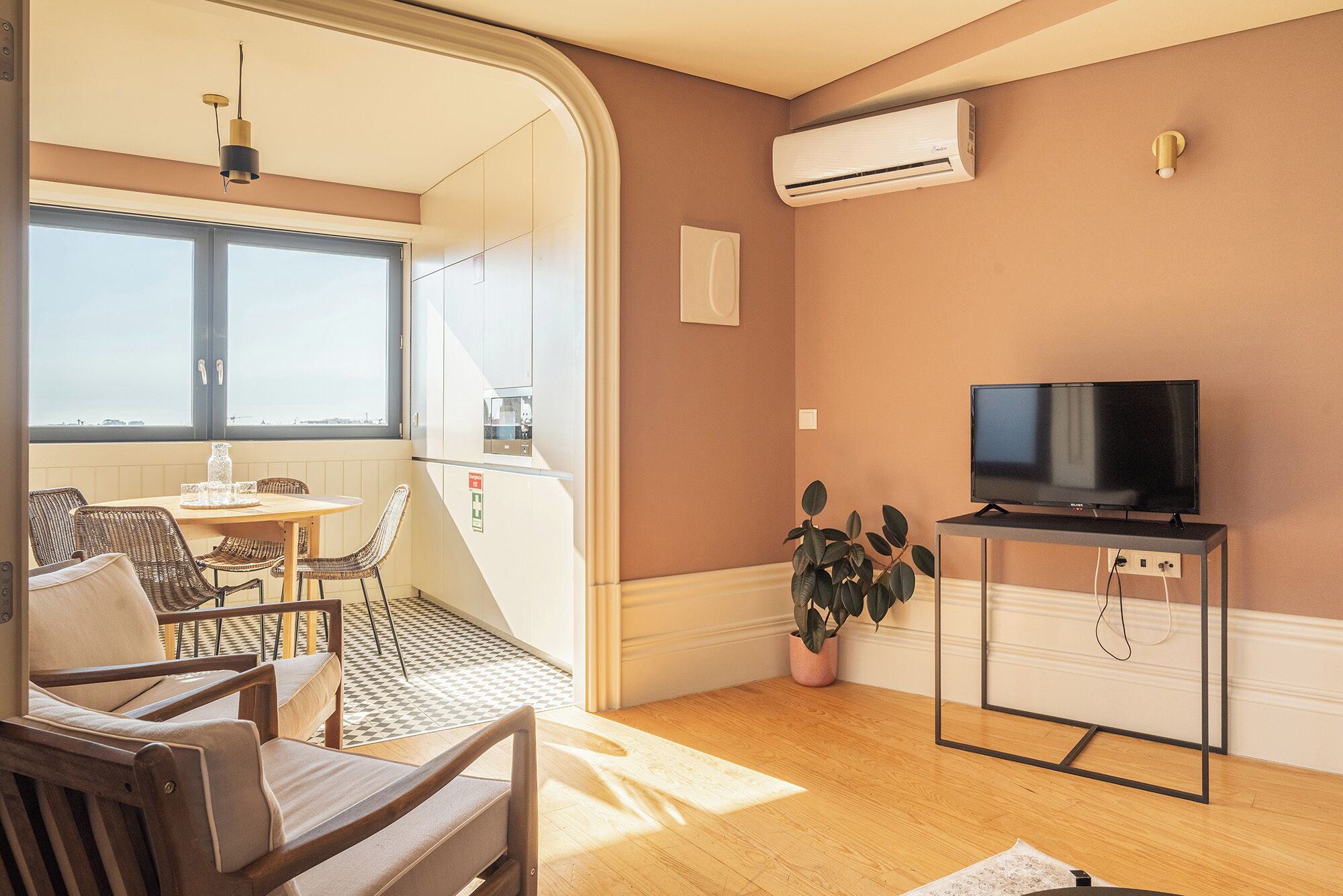 Una sala moderna con televisor de pantalla plana, un comedor con sillas de mimbre y un amplio ventanal con vistas.