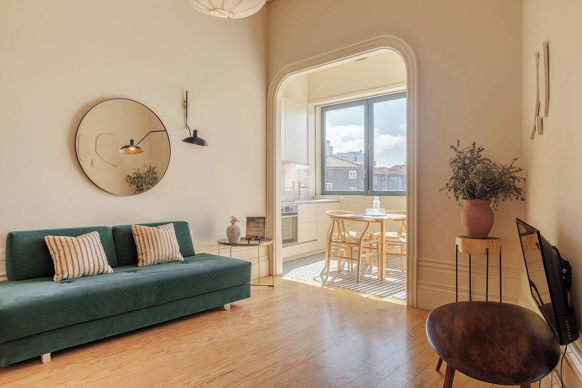 A modern living room with a green sofa, a round mirror, and a potted plant.