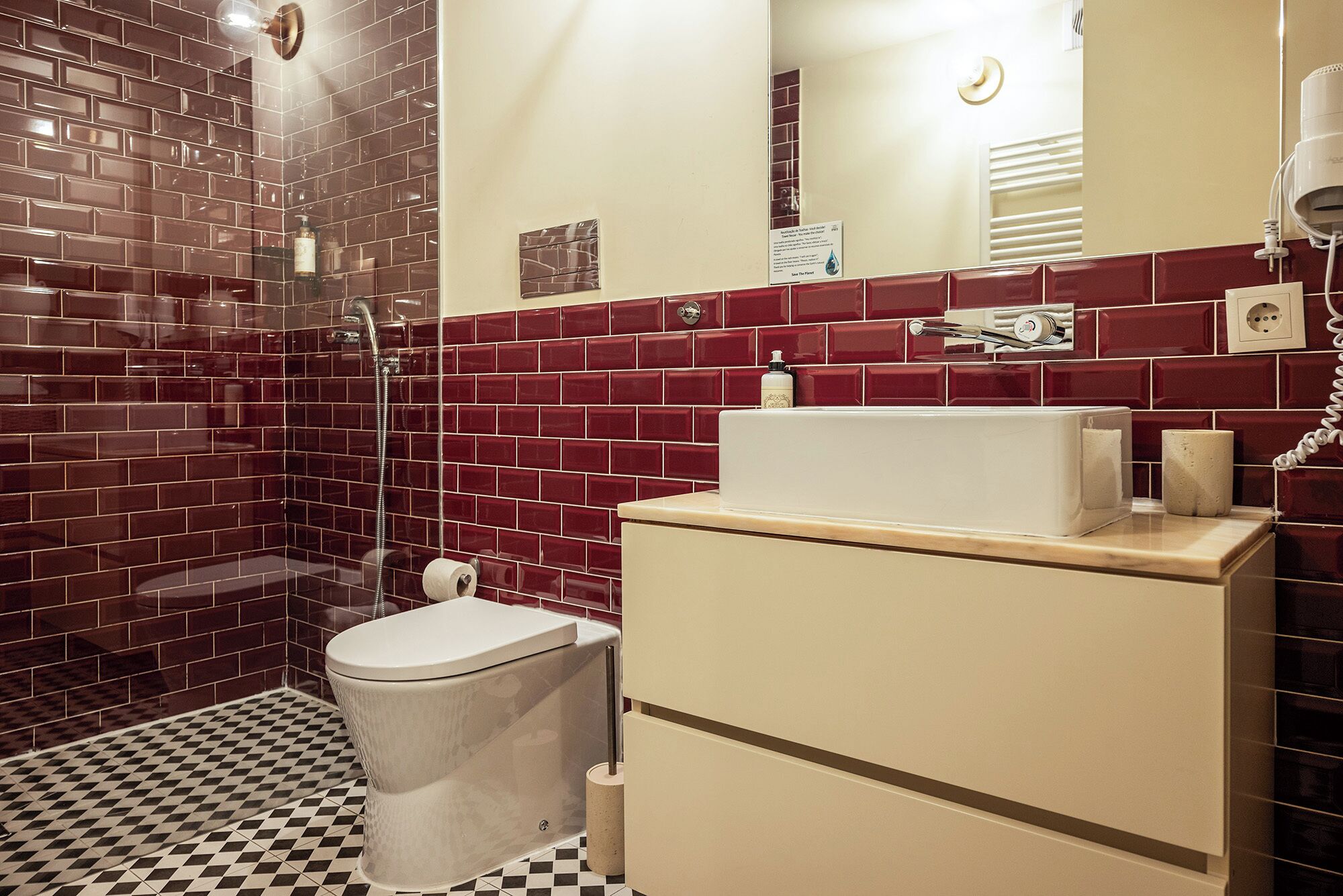 A bathroom with a toilet, sink, and shower. The walls are tiled in red and white, and there is a mirror above the sink.