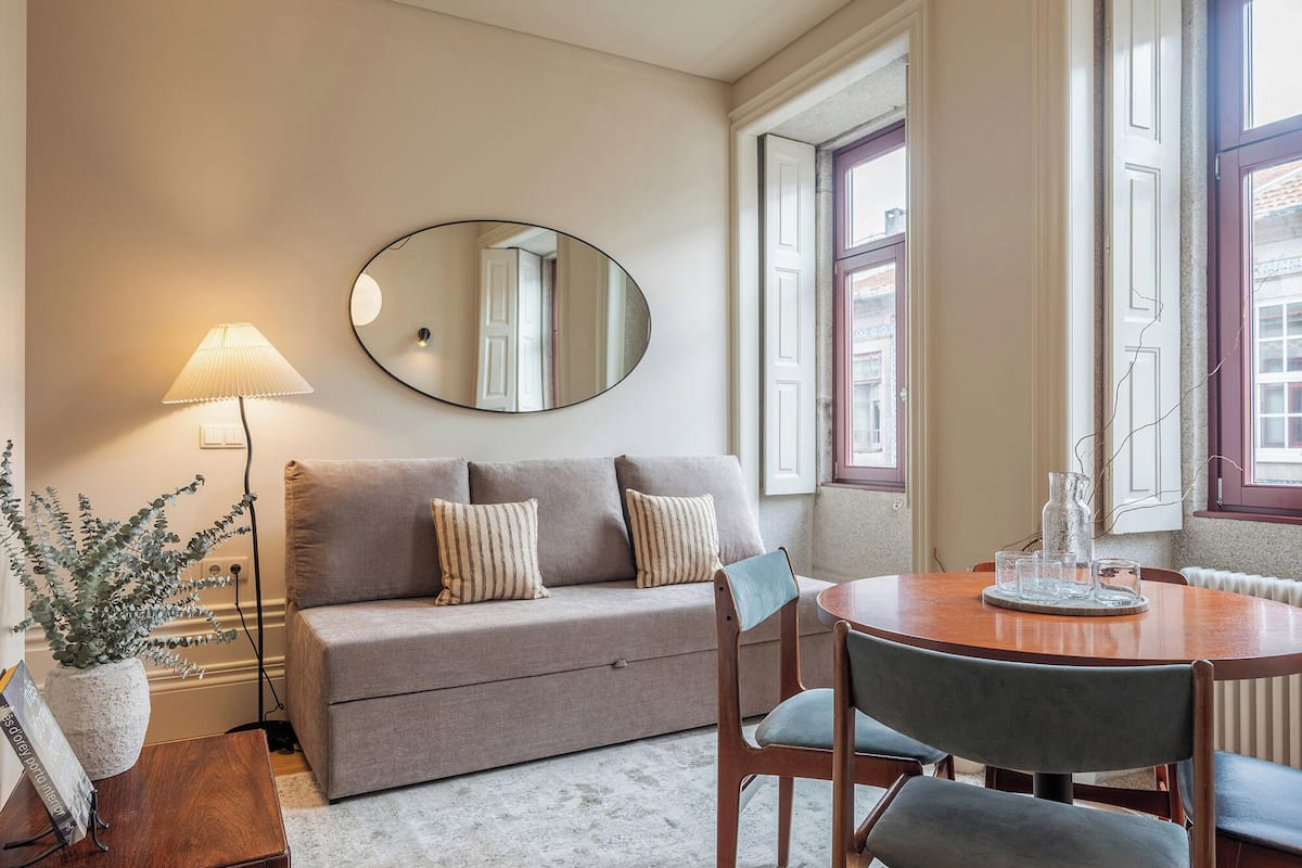 A cozy living room with a sofa, a round dining table, a lamp, and a mirror.