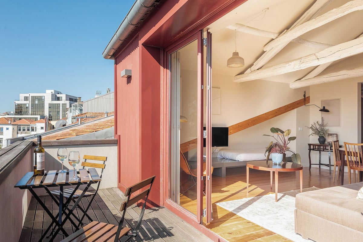 A balcony with a table and chairs, a sofa, and a bed in the adjacent room.