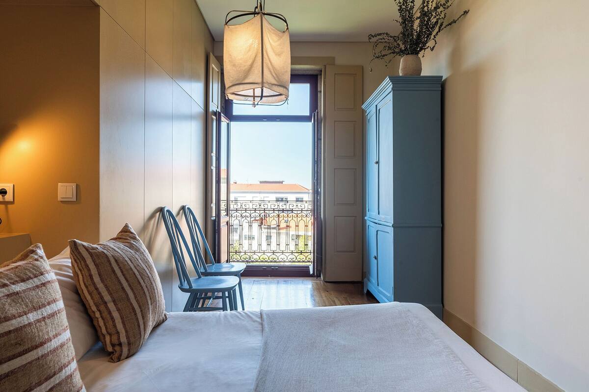 A hotel room with a bed, a blue wardrobe, a balcony with a view, and a hanging light fixture.