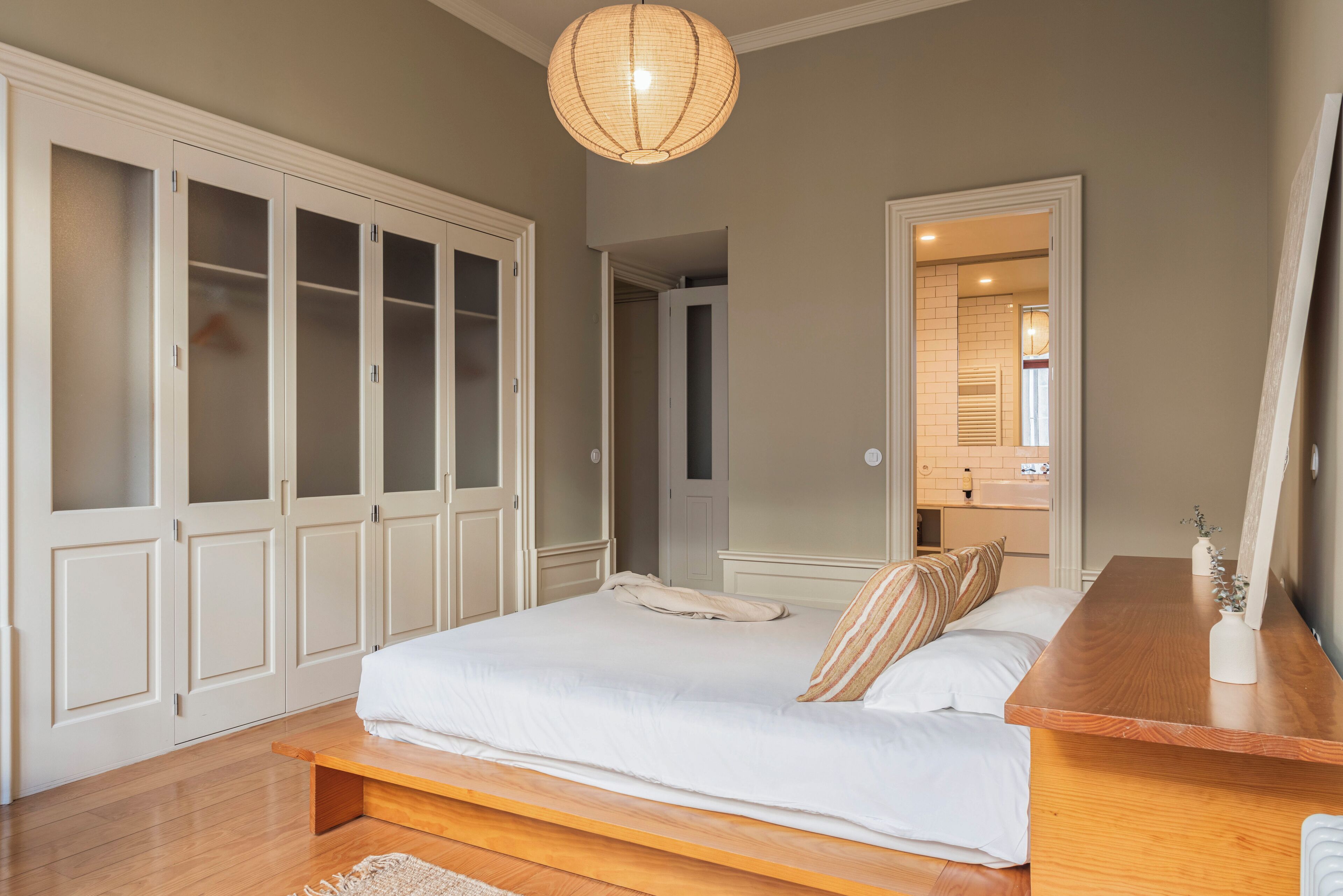 Un dormitorio con una cama grande, mesita de noche de madera y un armario con puertas de vidrio.