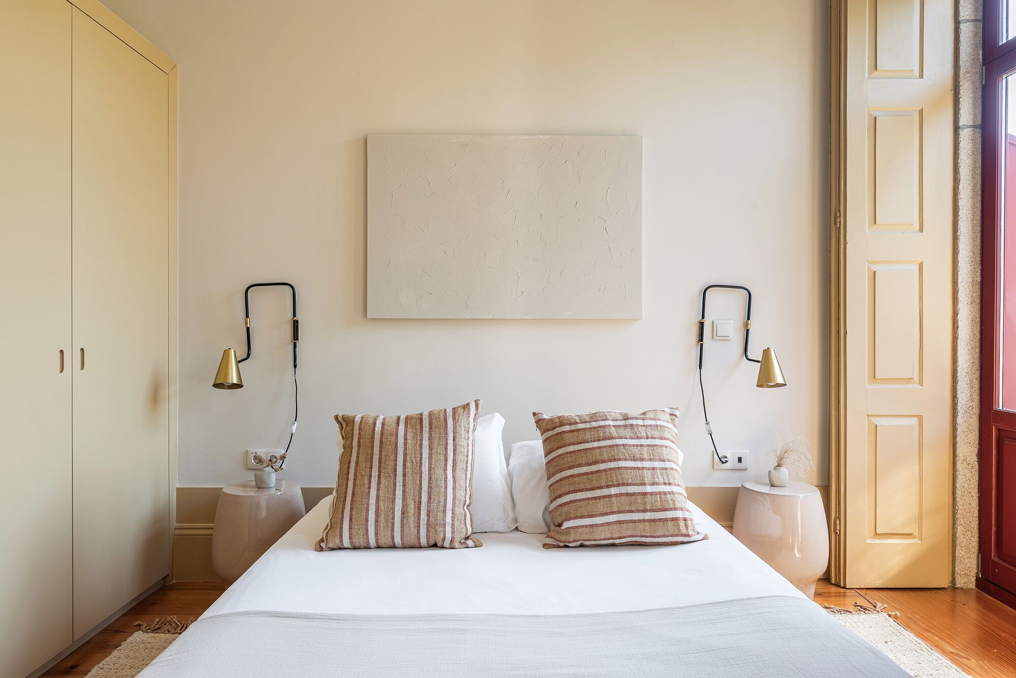 A bedroom with a large bed, two bedside tables, a wall-mounted lamp, and a door.
