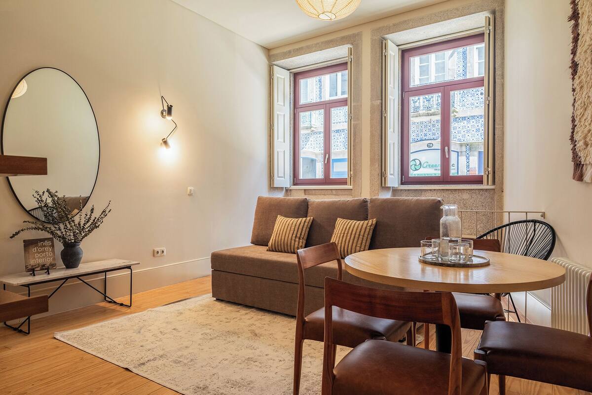 A cozy living room with a brown sofa, a round wooden dining table, and a large mirror.
