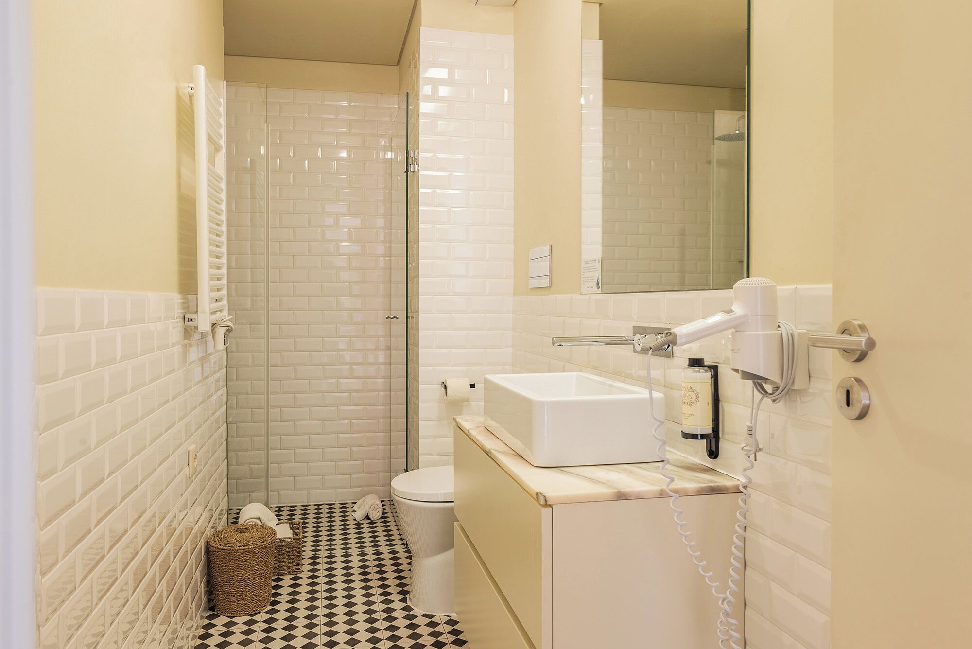 Een kleine badkamer met toilet, wastafel en douche. Handdoekhouder en spiegel boven de wastafel.