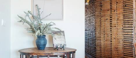 A wooden floor, a round table with a vase of plants, a black desk lamp, and a framed picture on the wall.