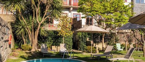 A swimming pool surrounded by grass and trees, with lounge chairs and umbrellas.