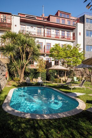A swimming pool surrounded by grass and trees, with lounge chairs and umbrellas. - Oporto Maison Alves da Veiga (Porto)