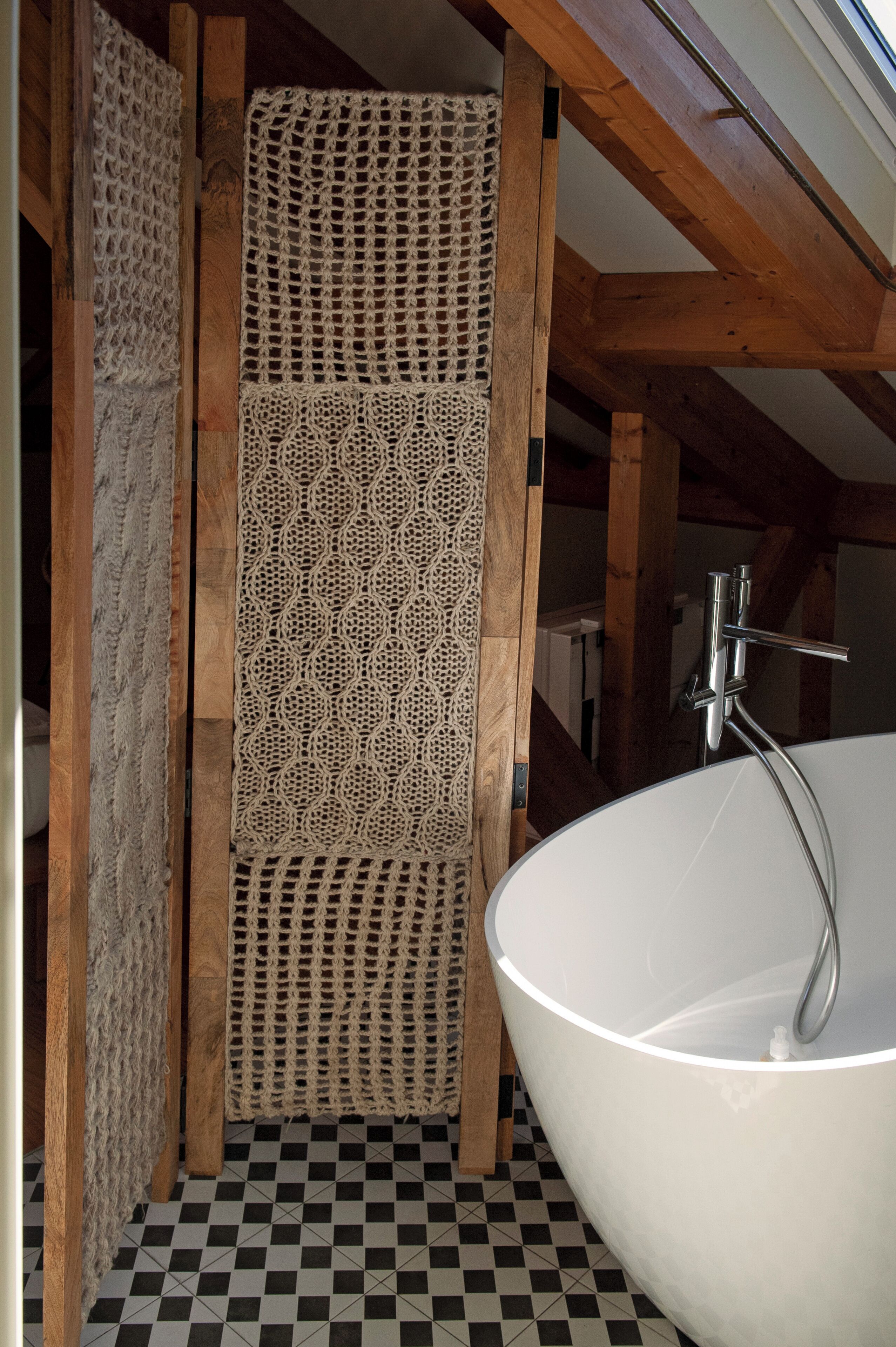 A bathroom with a large bathtub, wooden beams, and a checkered floor.