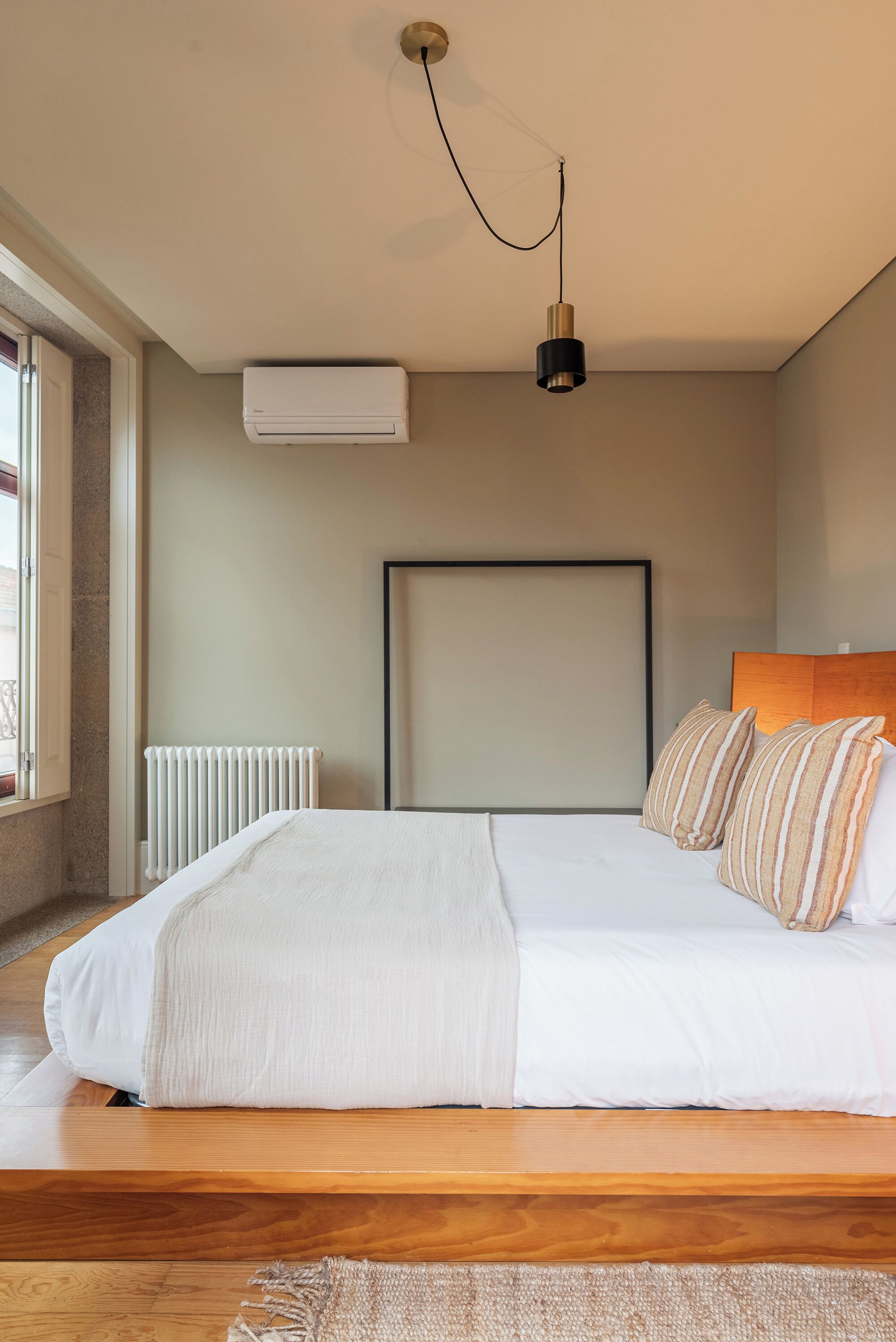 Un dormitorio con una cama grande, un radiador, un aire acondicionado y una lámpara colgante.