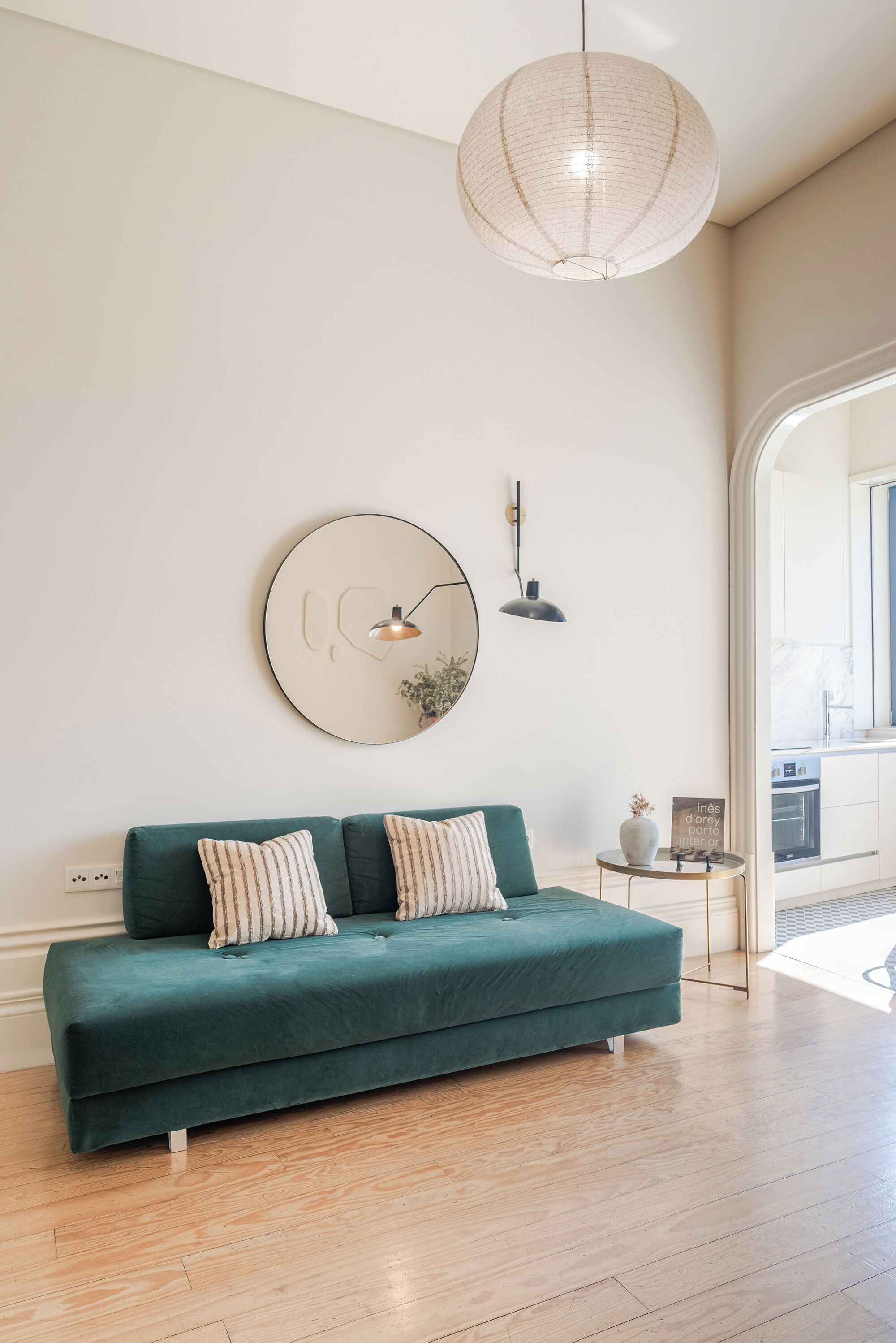 Una sala de estar moderna con un sofá color aguamarina, un espejo redondo y una lámpara colgante.