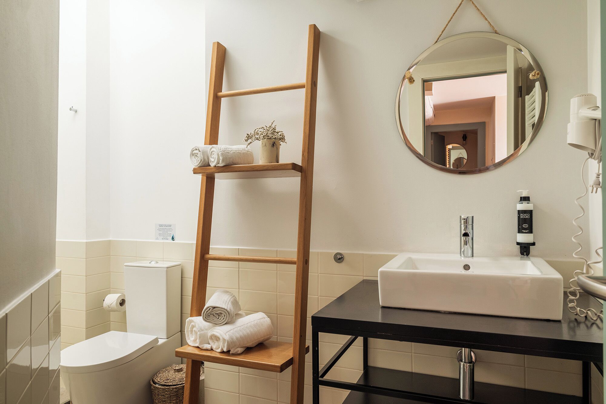Ein Badezimmer mit einer Holzlade, die Handtücher und eine kleine Vase beherbergt, einem weißen Waschbecken mit Spiegel darüber und einer Toilette.