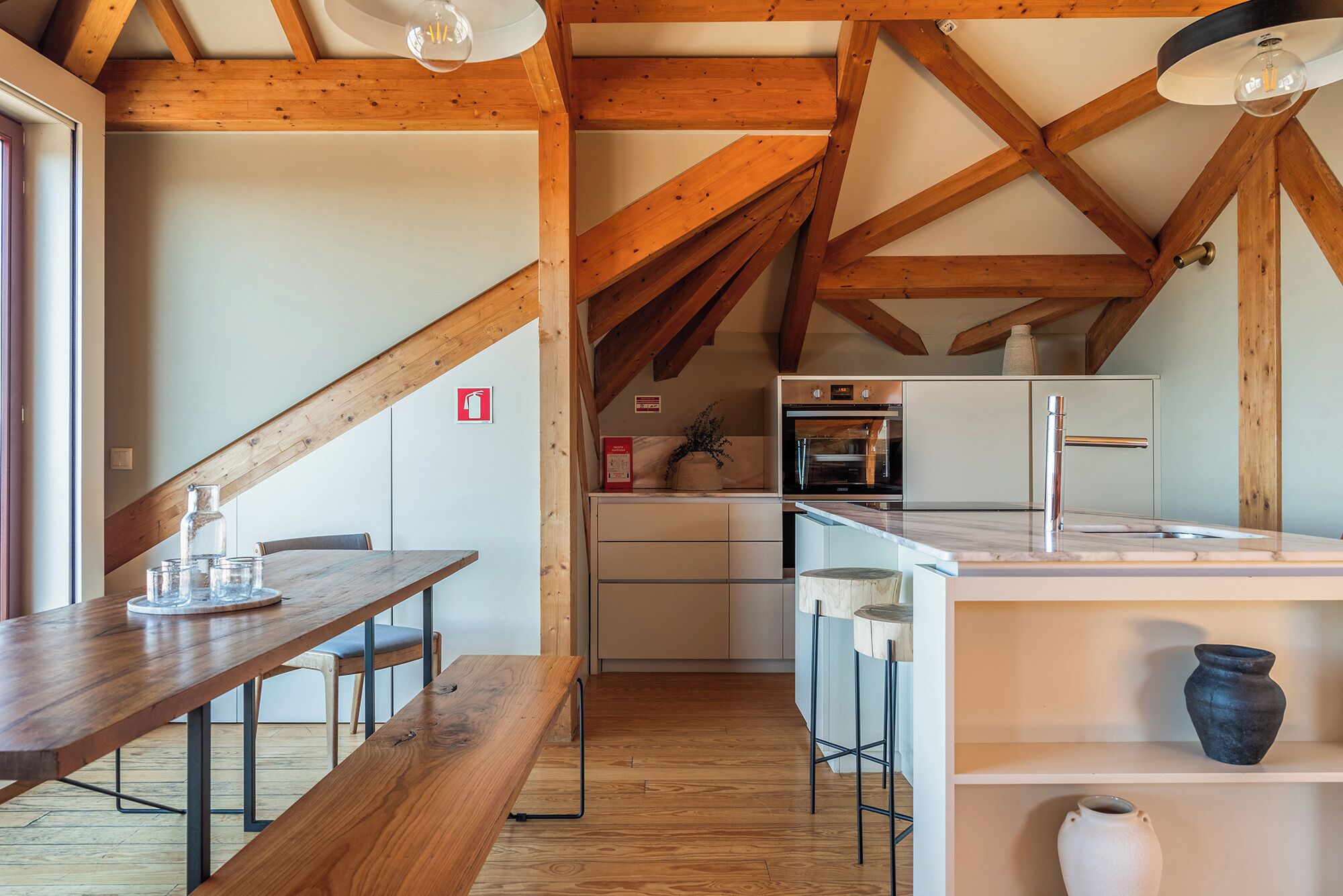 A kitchen with wooden beams, a dining area with a bench, and a small island with a sink.