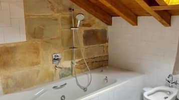 Une salle de bain avec une grande baignoire, une douche et des toilettes. Les murs de la pièce sont en pierre et le plafond est orné de poutres en bois.