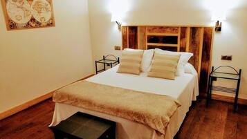 Un dormitorio ordenado con cama, mesitas de noche, un pequeño banco y una obra de arte colgada en la pared.