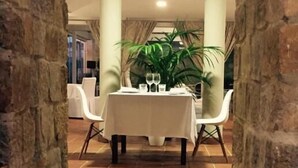 A dining area with a table set for two, flanked by stone pillars, and a potted plant in the center. - Hotel Palacio de Arce (Pielagos)