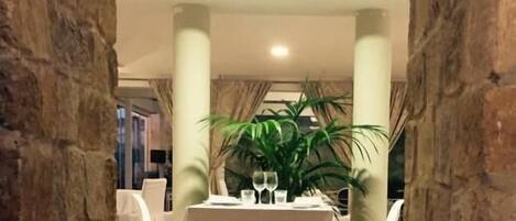 A dining area with a table set for two, flanked by stone pillars, and a potted plant in the center.