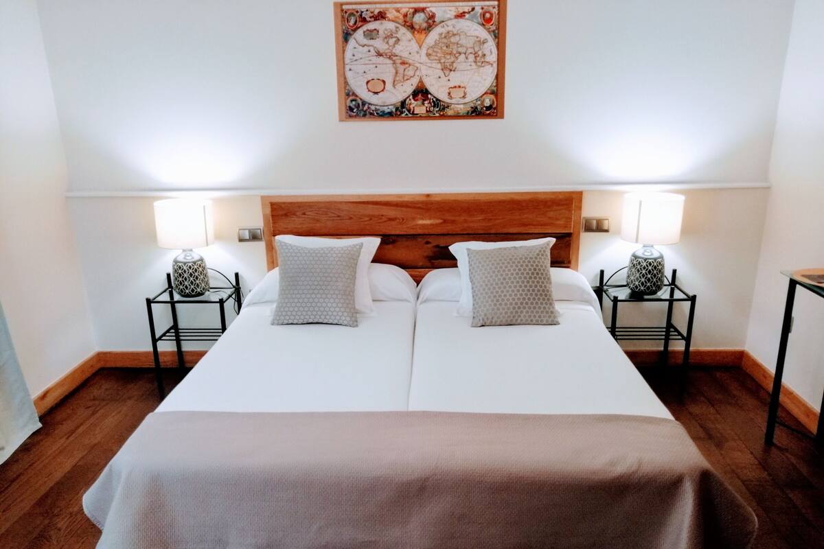 A double bed with a wooden headboard, two bedside tables with lamps, and a decorative wall piece above the bed.
