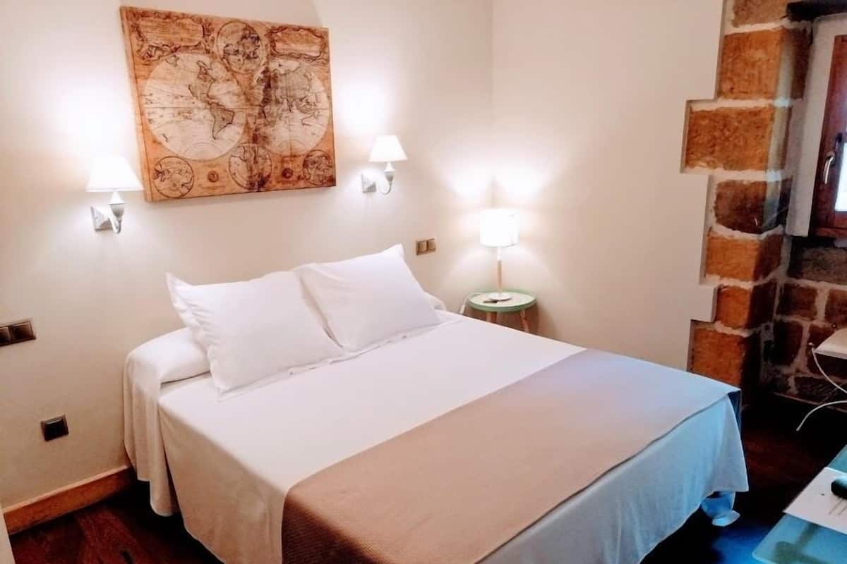 A neatly made bed with white linens, a large map artwork on the wall, and a small table with a lamp beside it.
